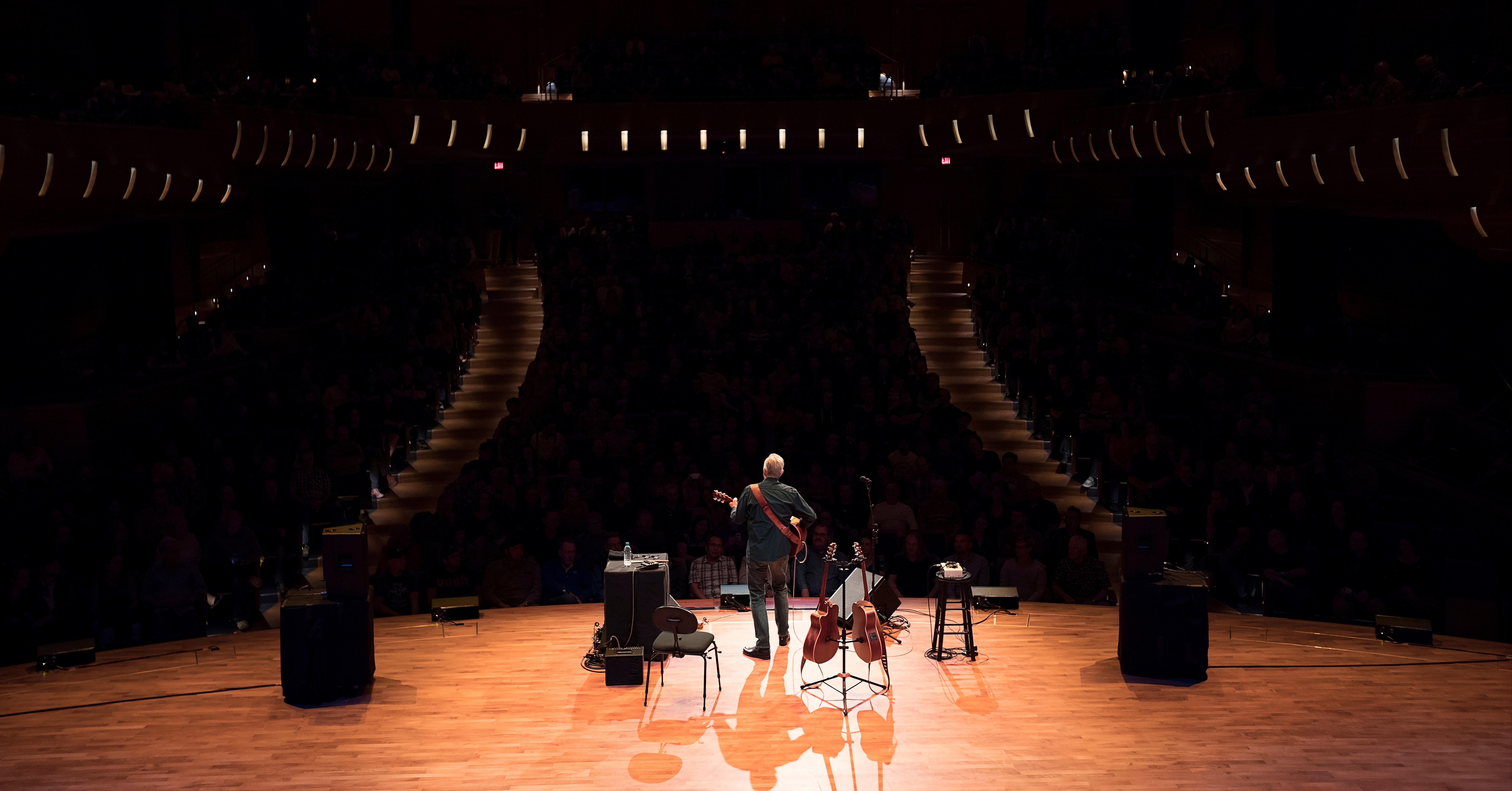 A man, viewed from behind, playing the guitar on the stage of the Bella Concert Hall